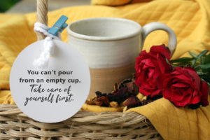 A paper reads, "you can't pour from an empty cup. Take care of yourself first." attached to a coffee cup with two roses in a basket. This reflects concepts discussed in counseling for moms in Denver, CO with Hot Mess Counseling. Stressed out moms need tips for coping with anxiety and stress in Lakewood, Denver, Morrison, Littleton and beyond with online therapy in Colorado.